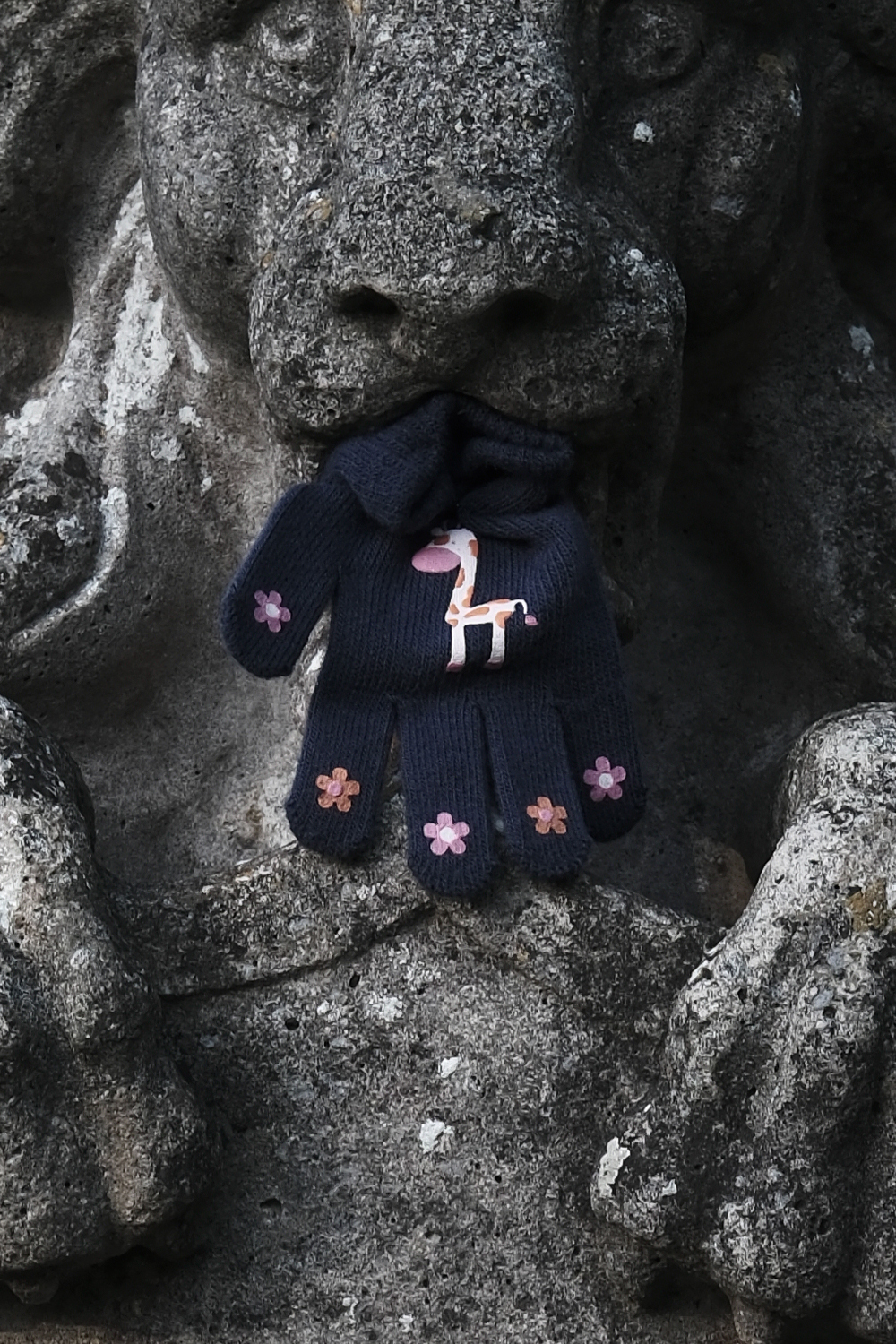 A photo of a child's glove in the mouth of a stone lion sculpture. This is a very tight crop into the previous slide's image.