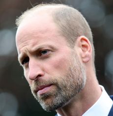 Prince William wearing a white shirt and blue jacket looking stern