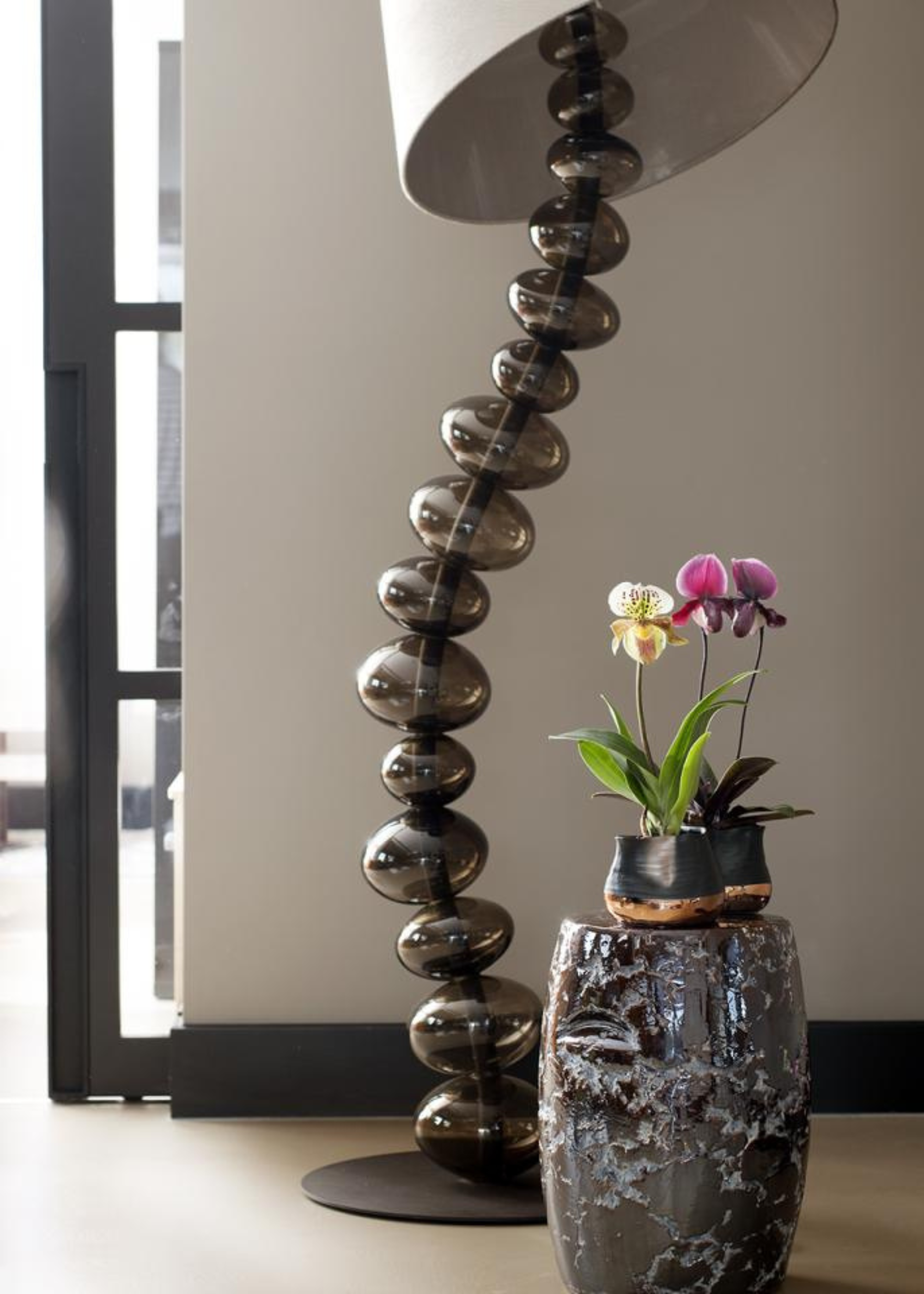 A pair of potted orchids on a pedestal near a wavy floor lamp