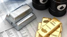 Gold and silver bars, as well as canisters of oil, rest on spreadsheets indicating commodity performance.