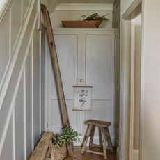 A neutral-painted narrow hallway with a panelled wall and a rustic bench