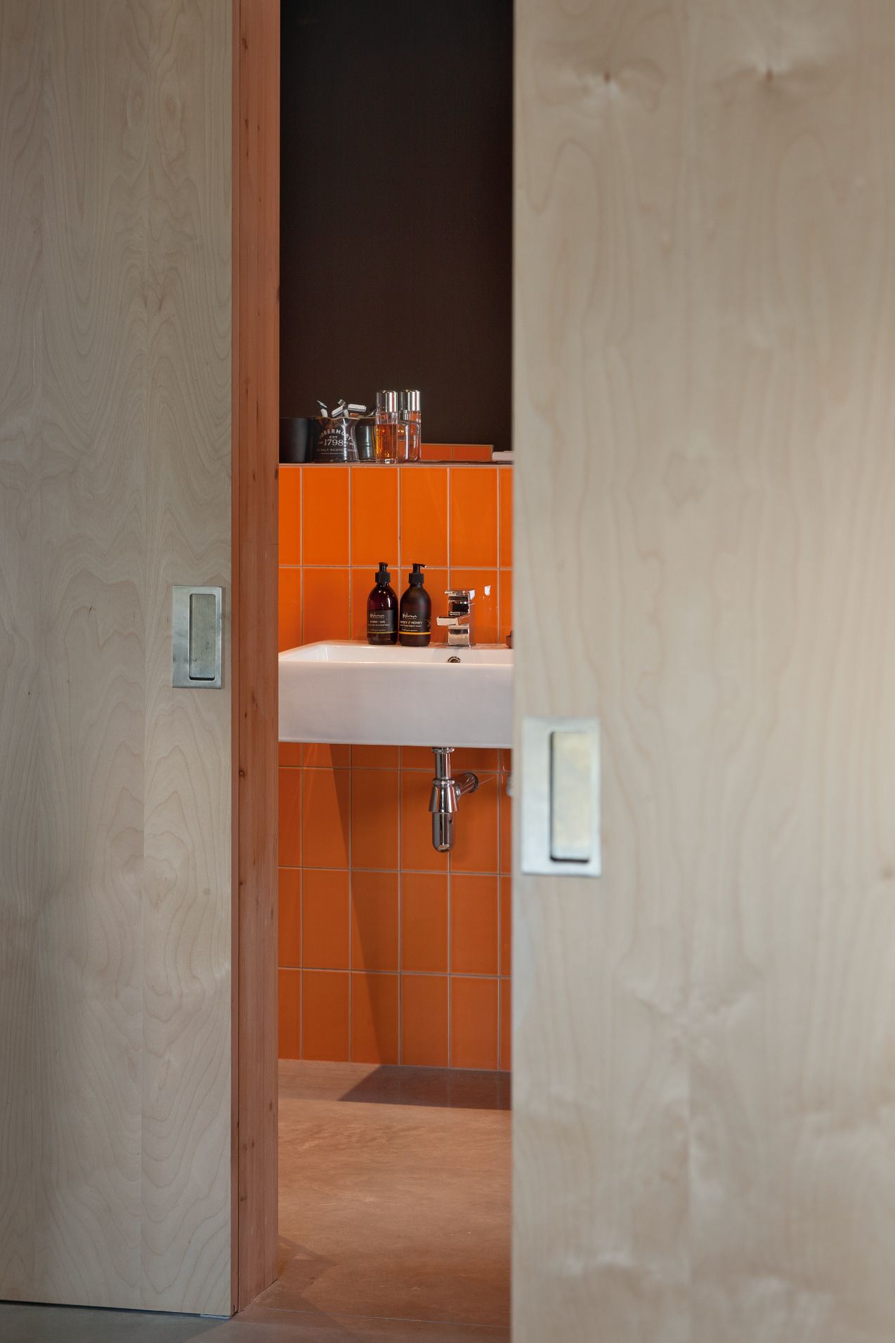 Plywood doors opening to reveal a bathroom with orange tiles and black walls