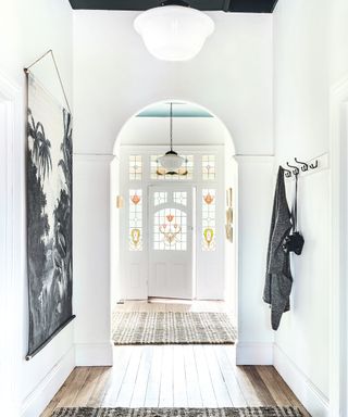 white hallway with door with stained glass windows, white pendant light and wooden floor