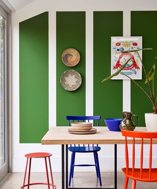 Green dining room, wooden dining table, colorful seating, artworks on walls