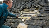 Roofer measuring hole in traditional stone tile roof 