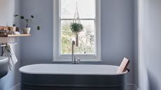 bathroom with light gray walls, large bath in front of window with hanging plant