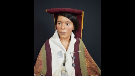 A model reconstruction shows a woman with short dark hair brushed under a red flat-top cap with a red and yellow dark veil behind it and a white and red cloak pinned to her body