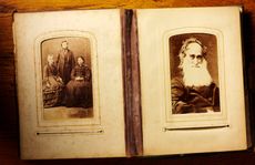 A picture of an antique photo album, likely from the Victorian era. The album is open to one page of a very old man with a long, white beard, and a page of three adults.
