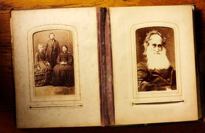 A picture of an antique photo album, likely from the Victorian era. The album is open to one page of a very old man with a long, white beard, and a page of three adults.