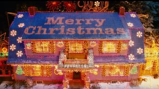 A house is covered in Christmas lights. There are snowflake shaped lights on the roof, Christmas trees on the front of the house and a string of lights on the roof spell "Merry Christmas".