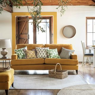 cottagecore decor ideas for living rooms, white farmhouse/cottage style living room with yellow accents, sofa and footstool, beams, rustic elements