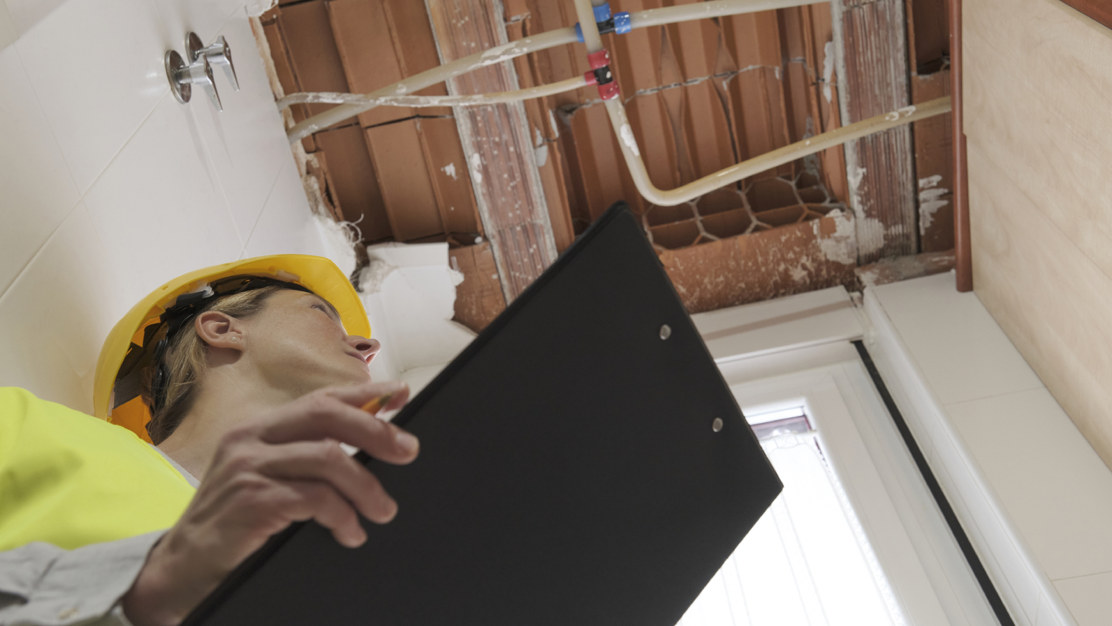 surveryor looking upwards to uncovered ceiling and pipework