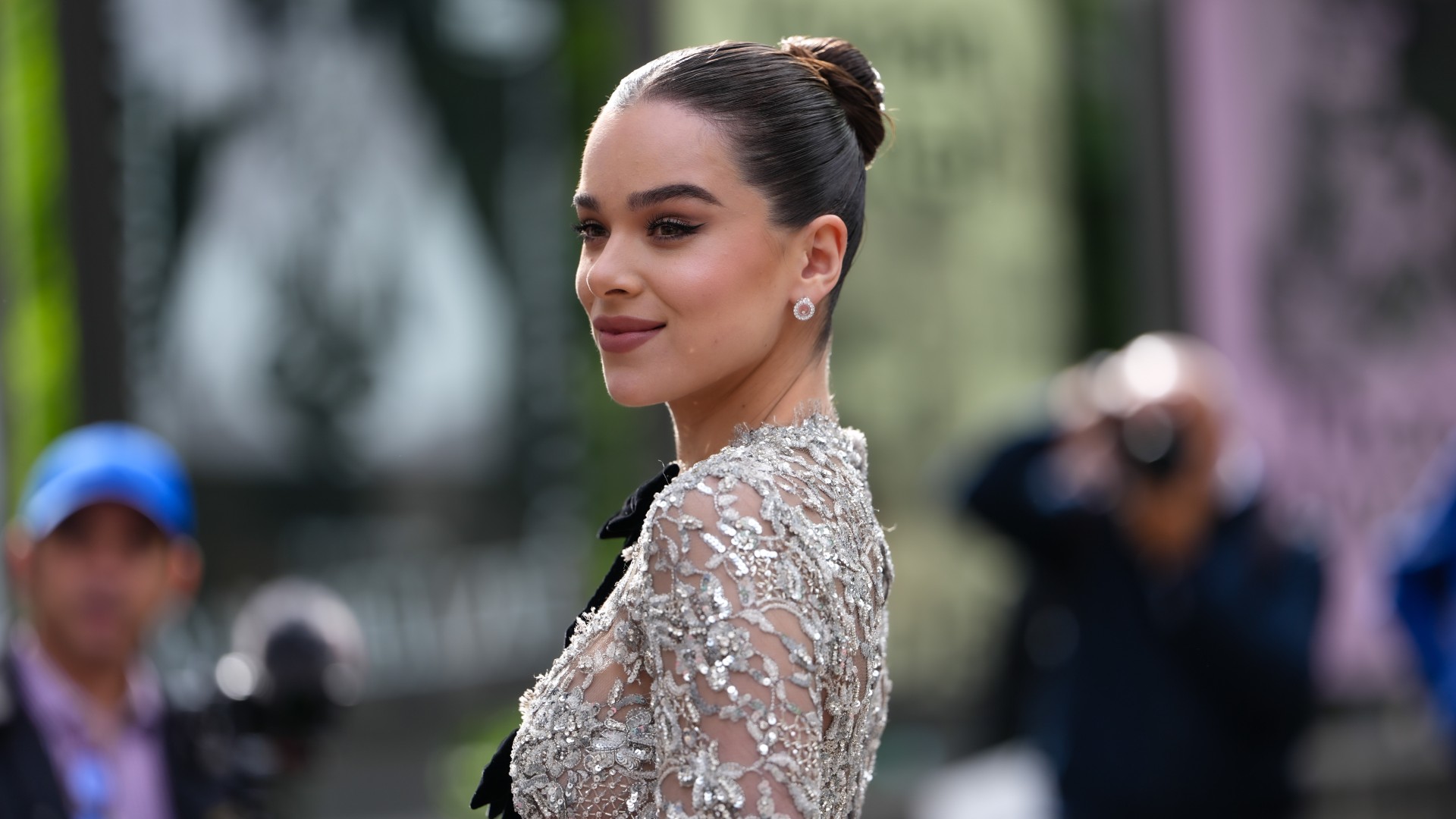 a white woman with dark hair pulled into a bun posing for paparazzi in a sequined mesh gown