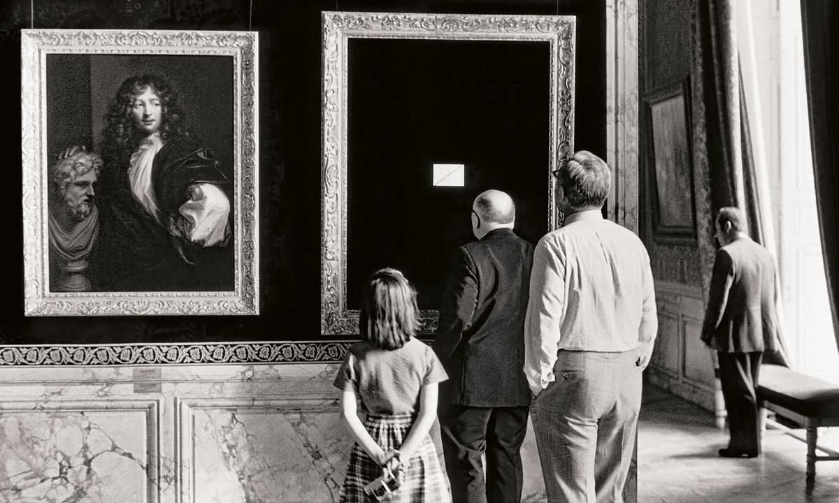 A group of visitors observes paintings in an elegant gallery with ornate frames and decorative walls, creating a classic museum atmosphere
