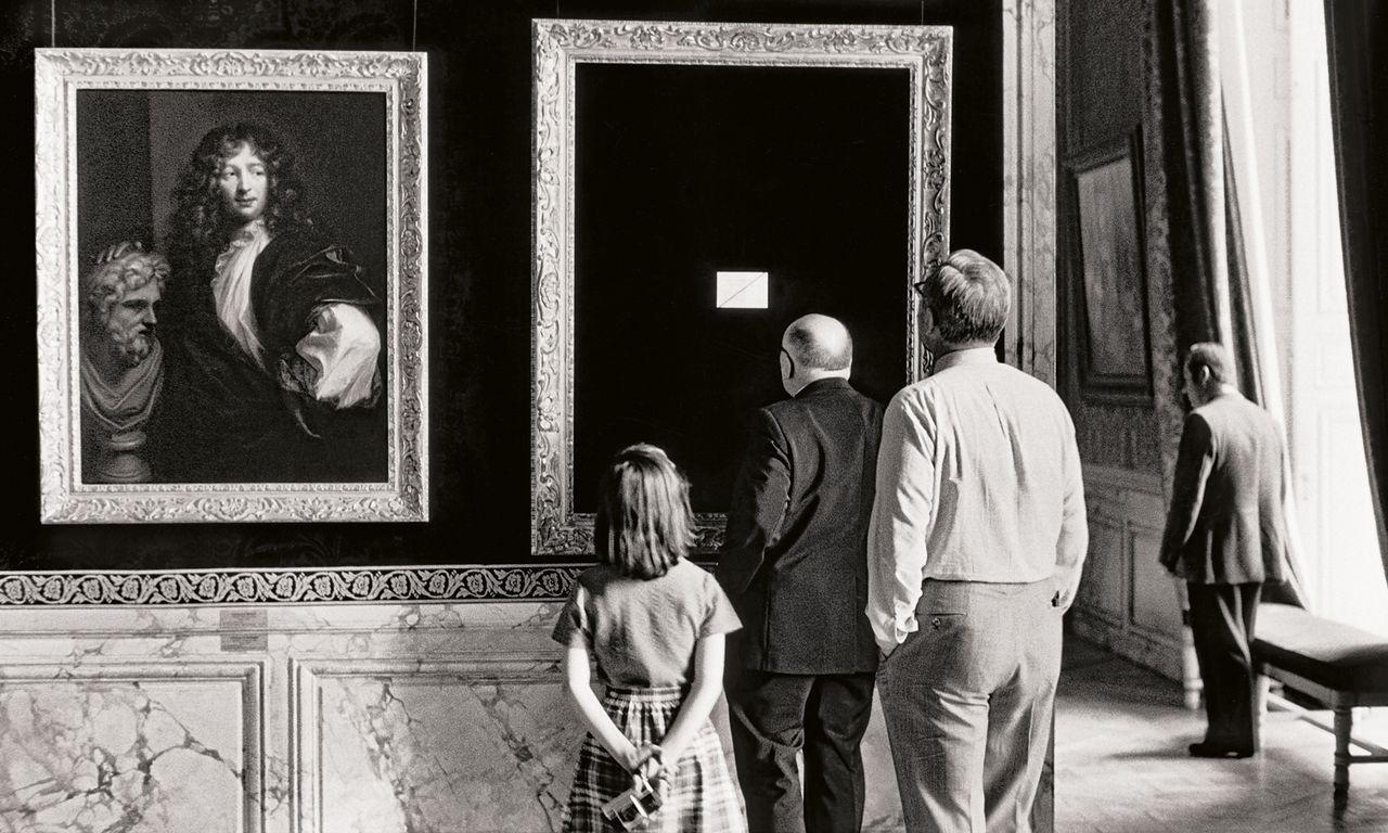 A group of visitors observes paintings in an elegant gallery with ornate frames and decorative walls, creating a classic museum atmosphere