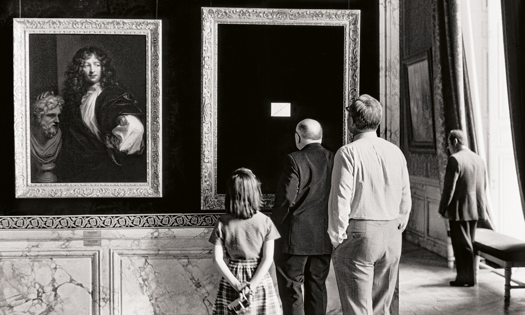 A group of visitors observes paintings in an elegant gallery with ornate frames and decorative walls, creating a classic museum atmosphere
