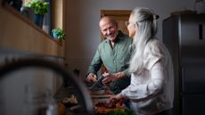An older couple smile at each other while preparing a meal together.