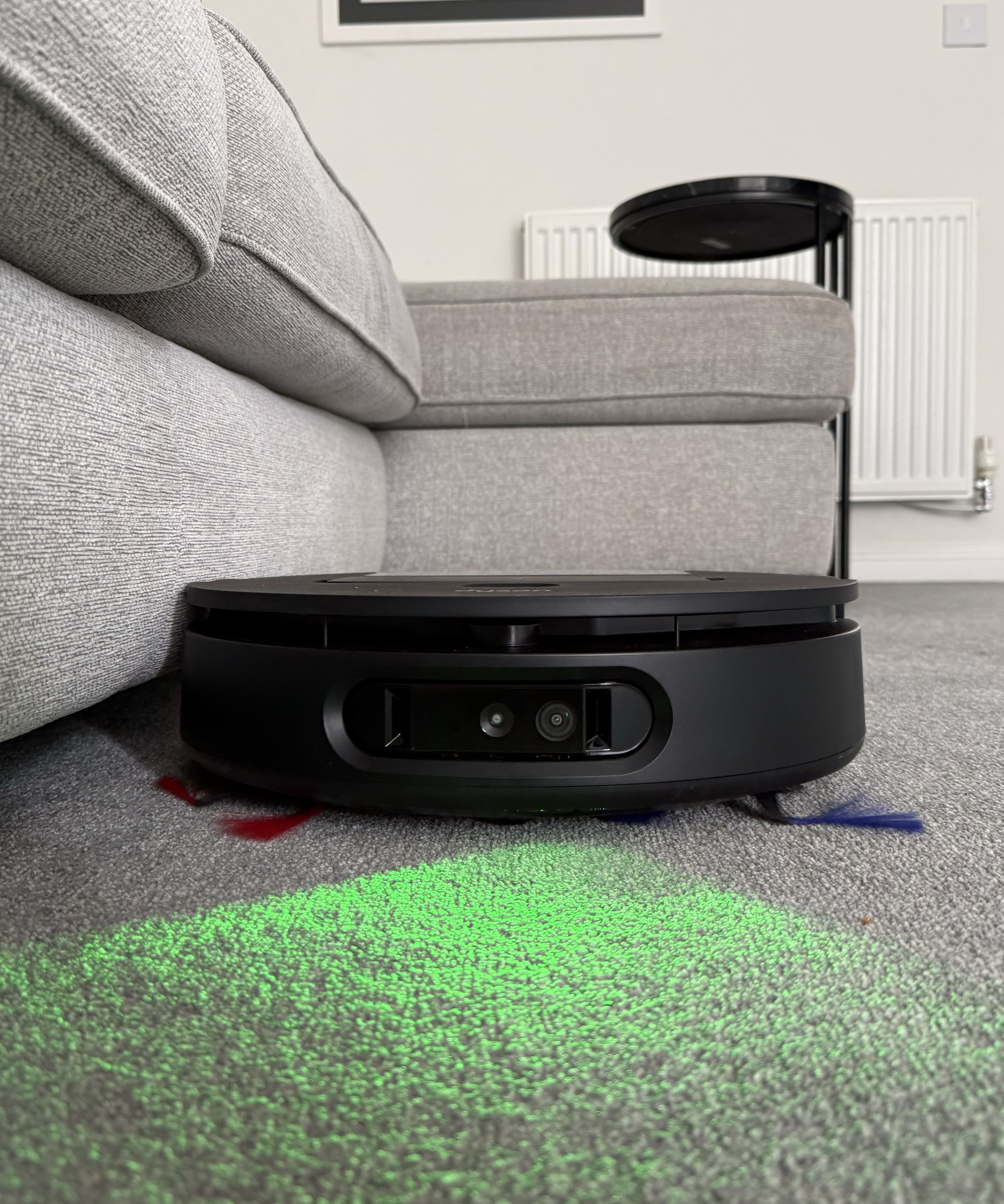 Dyson Spot+Scrub Ai cleaning under a sofa with green AI detection light visible on the carpet
