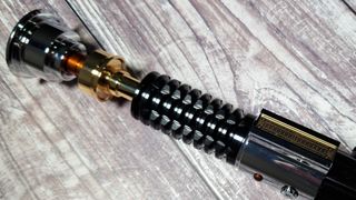 The hilt of the SabersPro Obi Wan EP3 lightsaber on a wooden surface