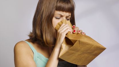 An anxious woman breathes into a paper bag.