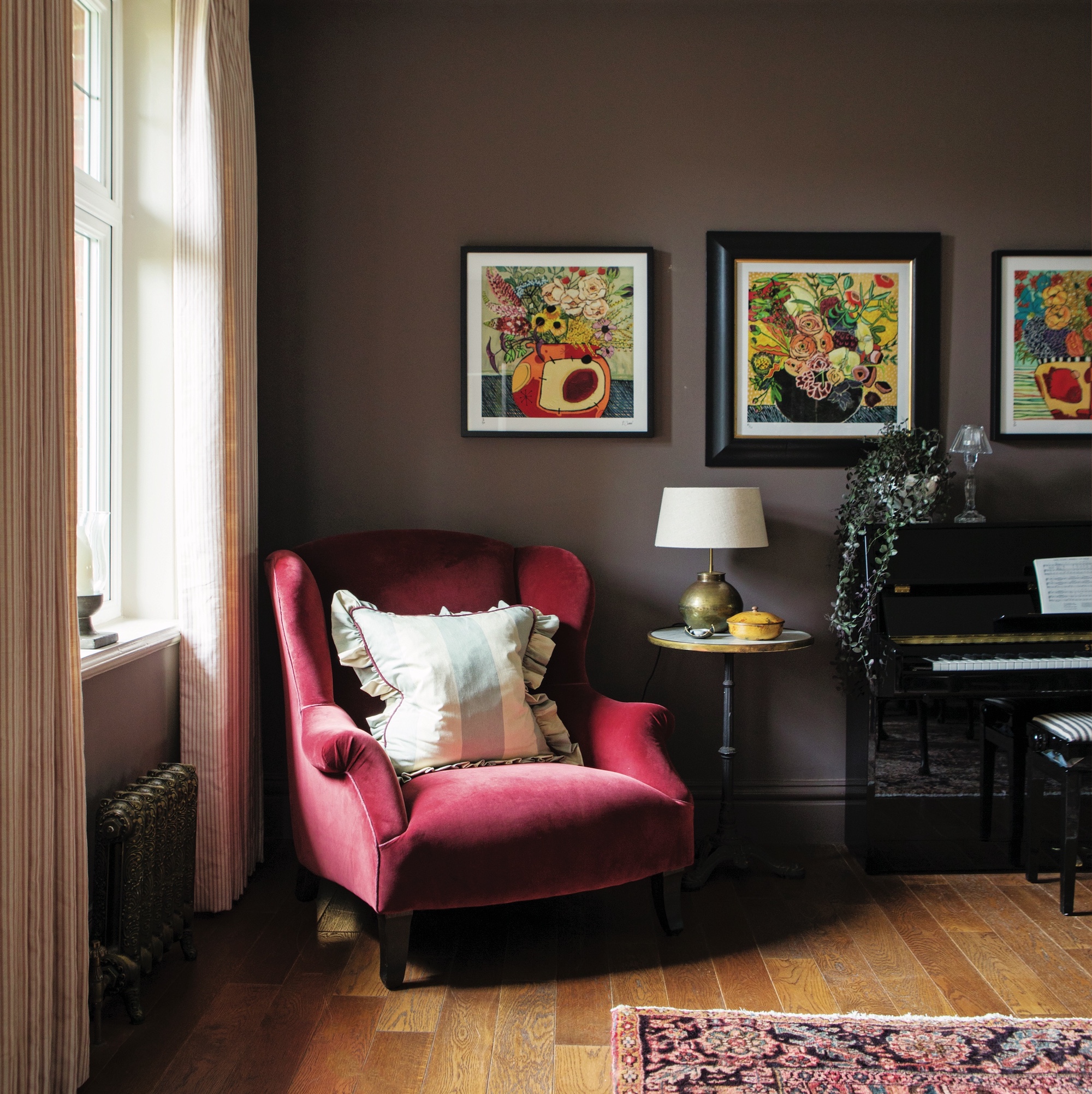 room with brown walls hung with flower paintings,and red velvet armchair with cushion with ruffle trim