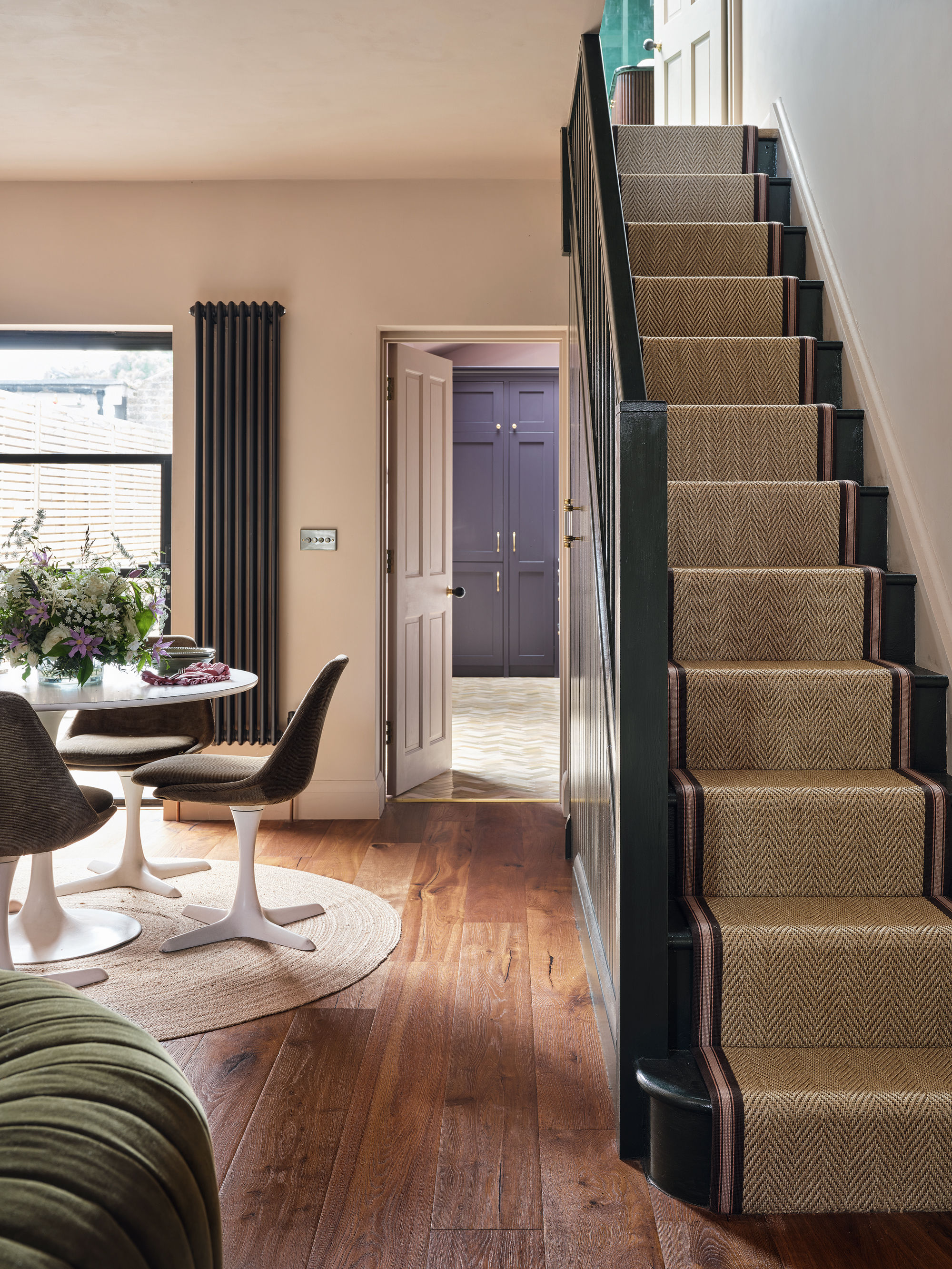 an open plan dining room with a Tulip table and matching upholstered chairs, fitted storage and a view into the kitchen and up the stairs