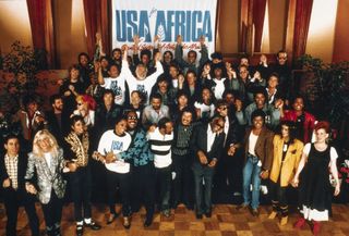a group photo of the artists who participated in recording "We Are the World," as they stand in front of a sign reading "USA Africa"