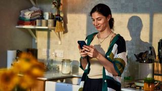 Woman standing with back against kitchen unit, looking at phone