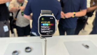 En Apple Watch Ultra med ett grått tygband hänger på ett ställ i en Apple Store.