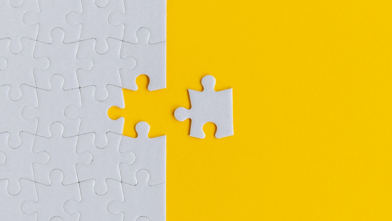 A white puzzle piece sits outside the rest of a puzzle against a yellow background.