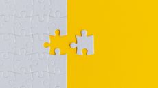 A white puzzle piece sits outside the rest of a puzzle against a yellow background.