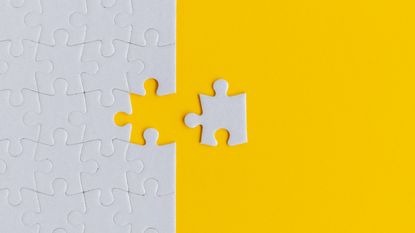 A white puzzle piece sits outside the rest of a puzzle against a yellow background.