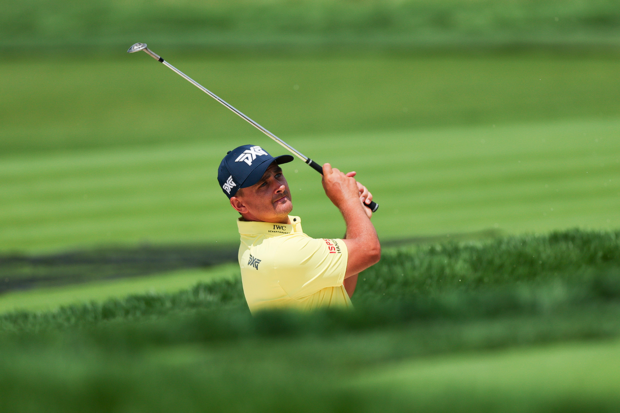 Christiaan Bezuidenhout hitting a bunker shot on the 7th hole hole at Oakmont during the US Open, with only the top half of his body visible due to the height of the lip on the bunker