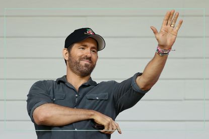 Ryan Reynolds waving at a football match wearing a Wrexham FC cap
