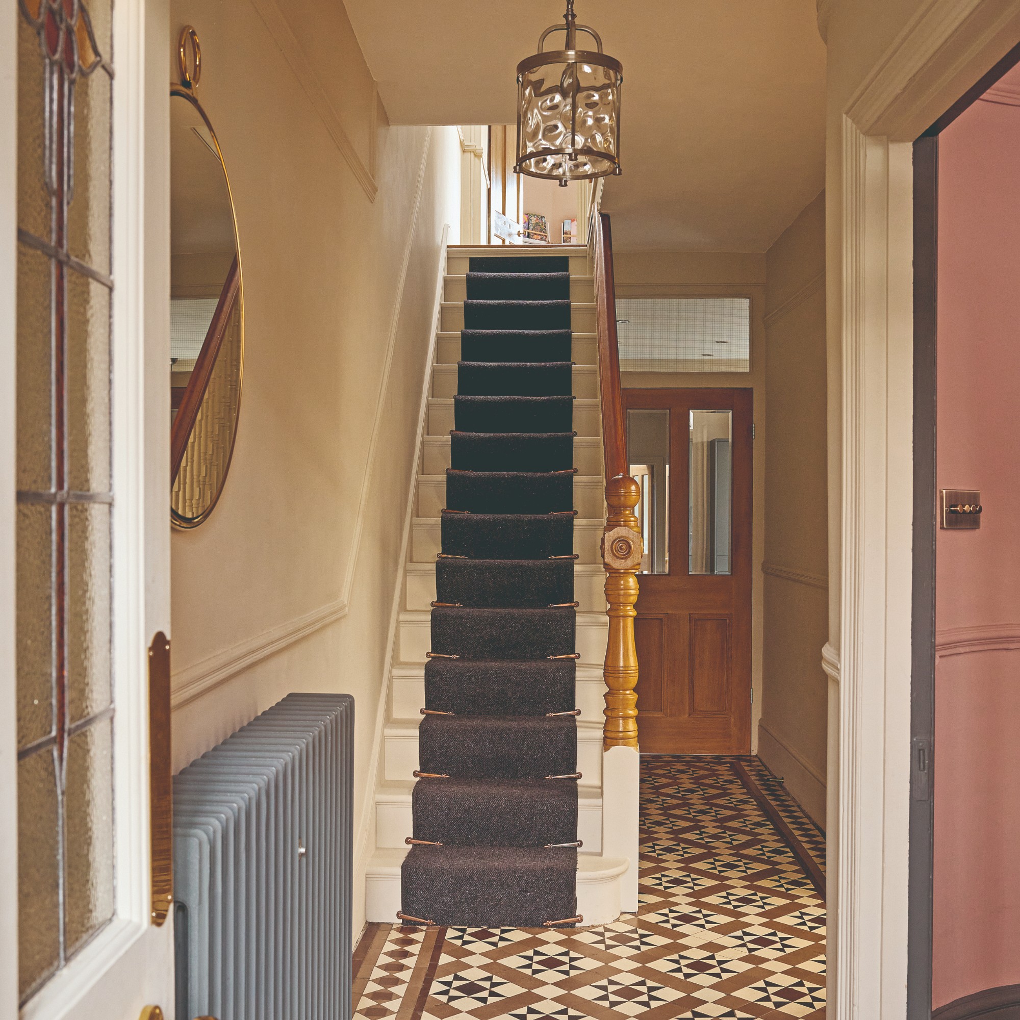 A soft, earthy pink-painted hallway with a staircase painted the same colour as the rest of the hallway and a black runner on top