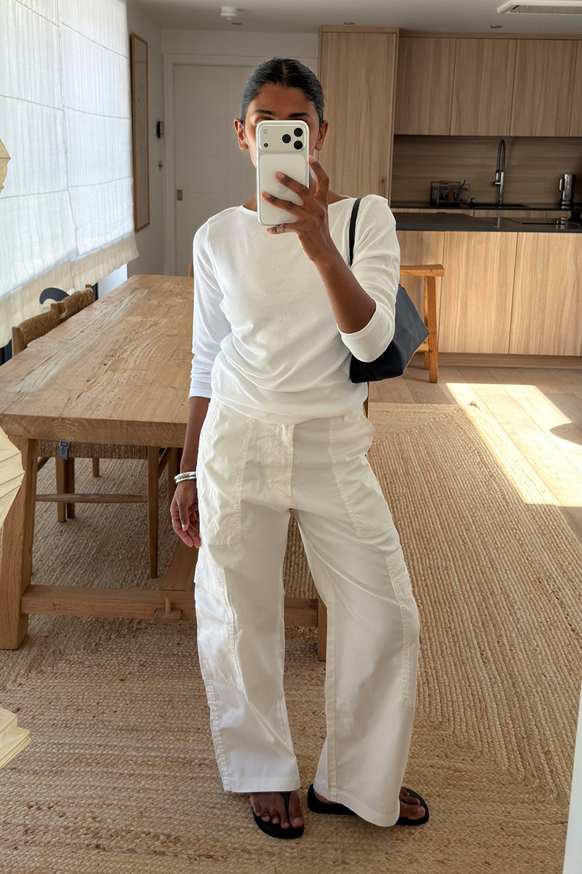 a woman wearing a white long sleeve top, white pants, and black flip flops