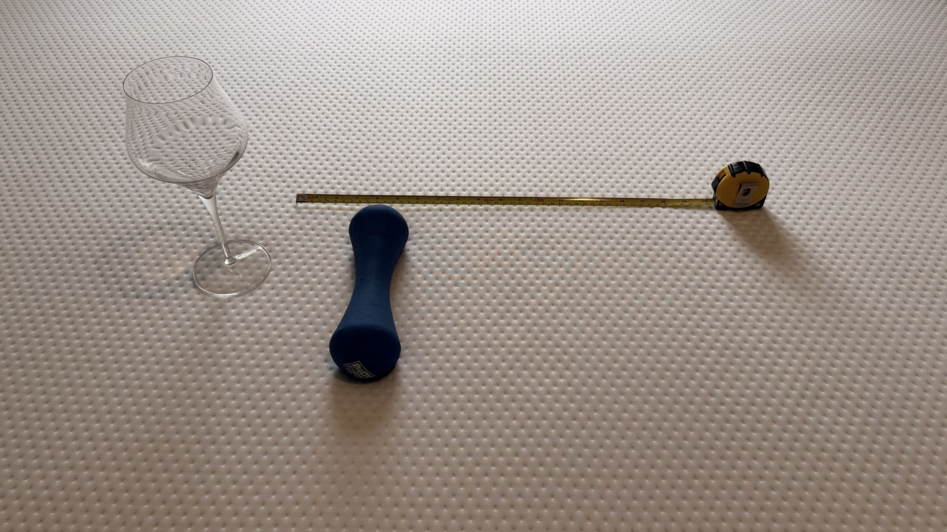 The image shows a blue weight next to an empty wine glass and measuring tape on top of a white mattress