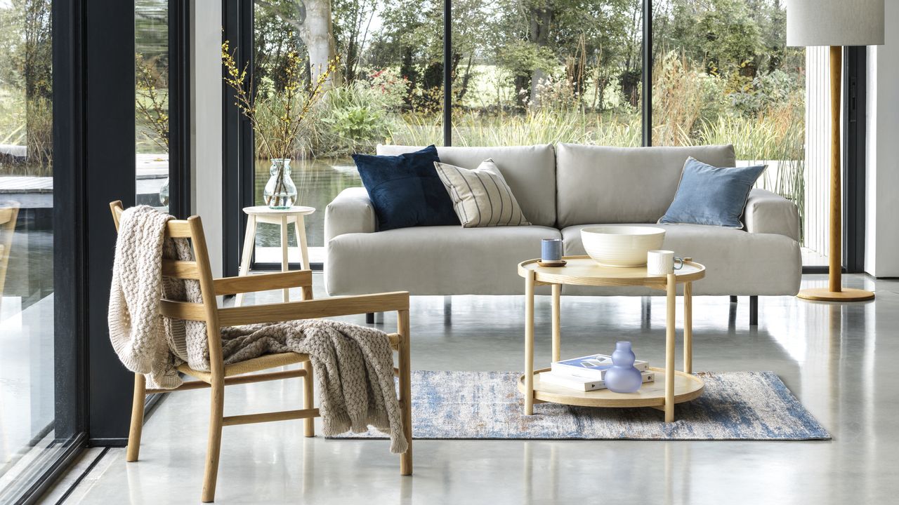 A cream sofa and wooden chair in a living area with glass walls