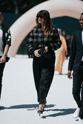 A woman at Paris Fashion Week wearing a flannel shirt outfit of a black and white plaid jacket, black pants, and black heels.