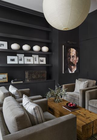 dark living room with paper pendant light, display shelves, four armchairs around a timber coffee table