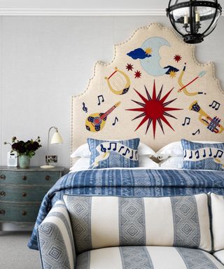 A bed with a large, cream headboard with musical instruments embroidered onto it