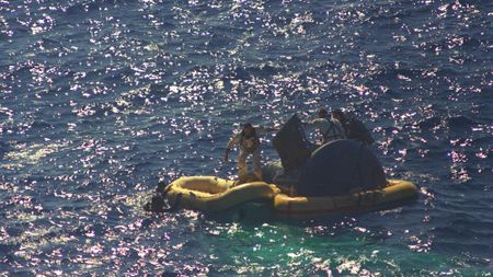Astronauts L. Gordon Cooper Jr. and Charles Conrad Jr. exit their spacecraft after splashdown of the Gemini-5 spacecraft. They are photographed boarding a life raft with the help of Navy divers.