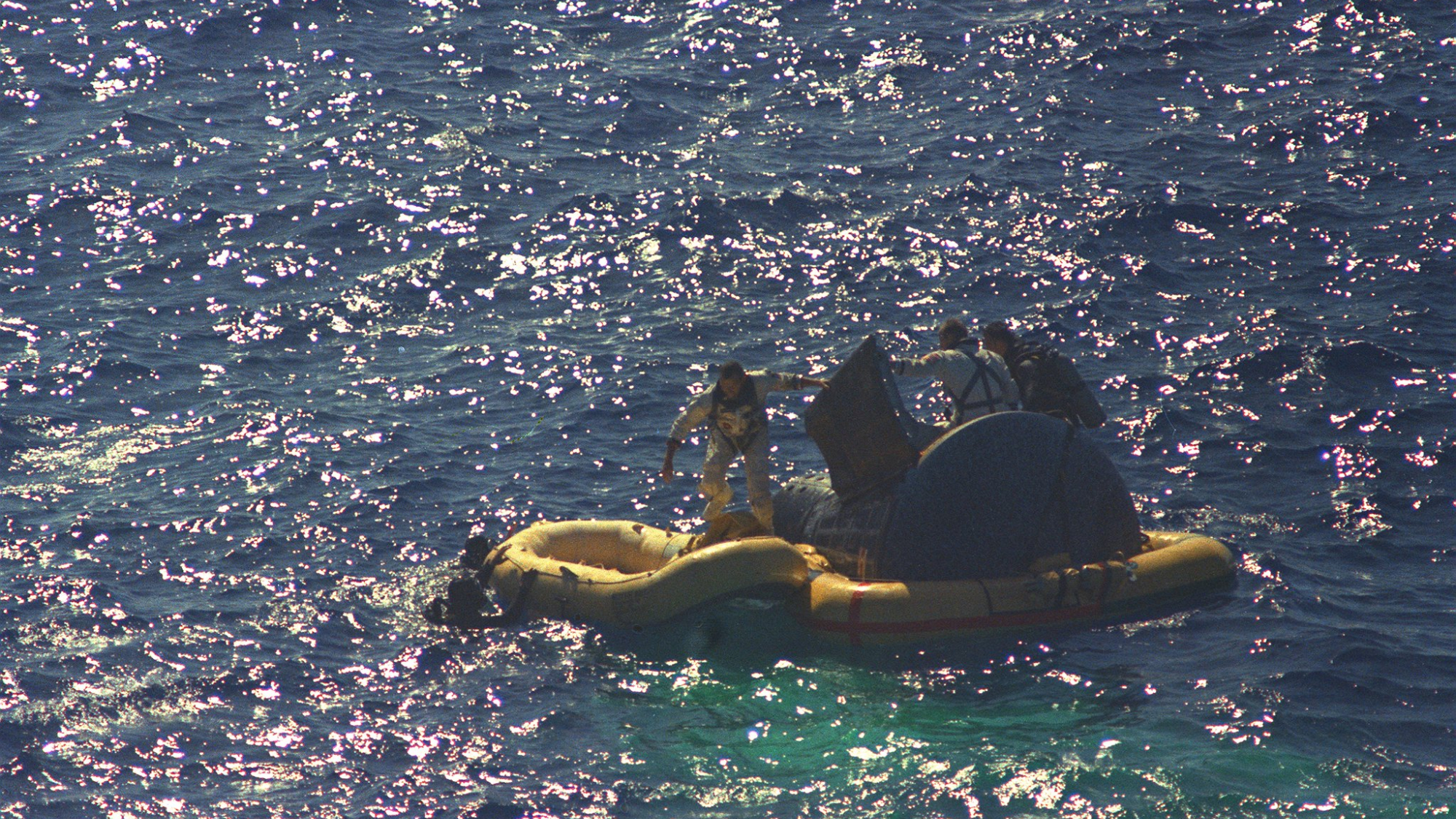 Astronauts L. Gordon Cooper Jr. and Charles Conrad Jr. exit their spacecraft after splashdown of the Gemini-5 spacecraft. They are photographed boarding a life raft with the help of Navy divers.