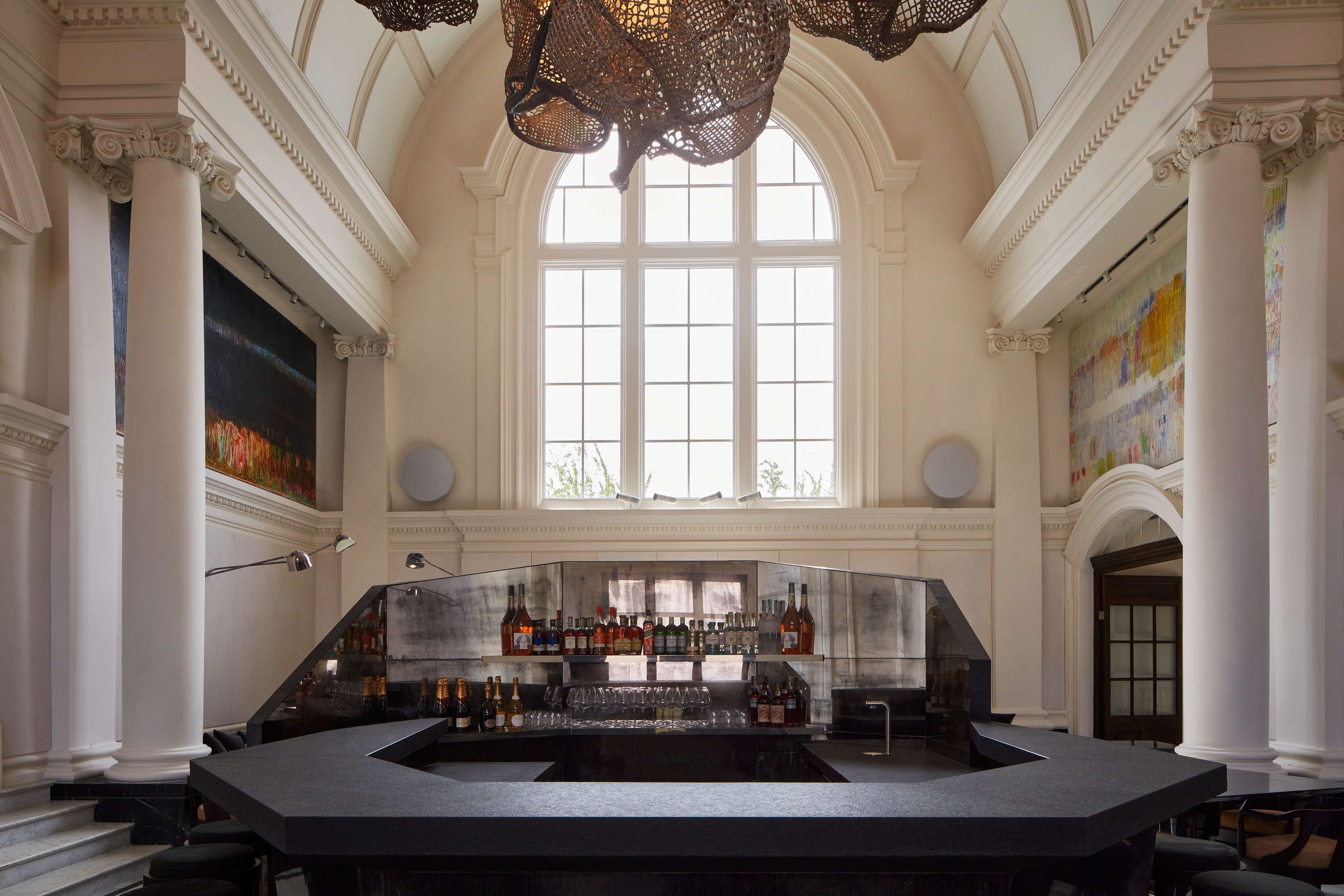 A palatial building houses a beautifully designed, chrome and black plaster sculptural bar counter above which floats a large-scale light installation.