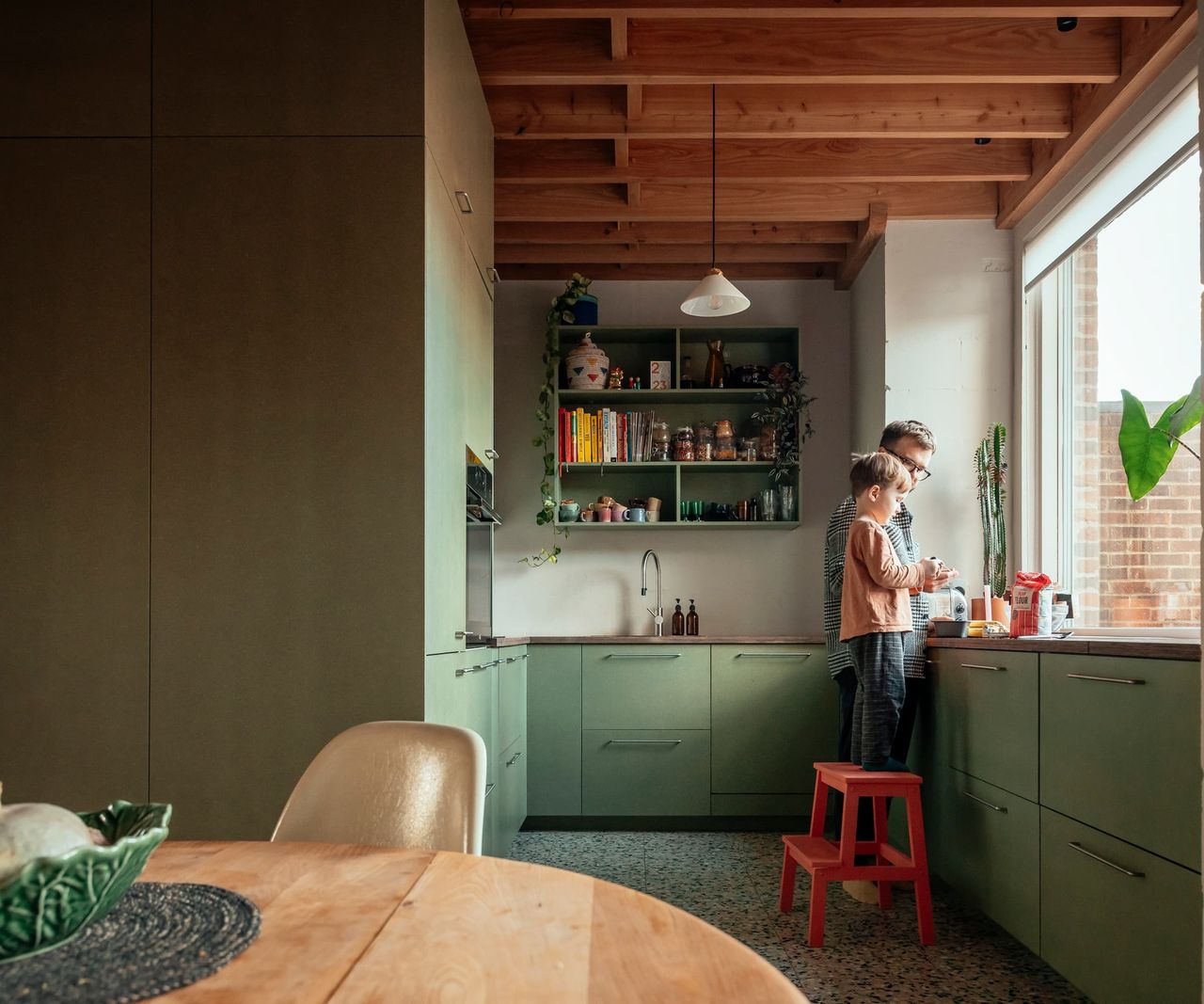 A kitchen with green cabinets and large picture window with wooden roofing