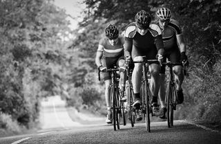 A black and white image of a group of road cyclists cresting a hill