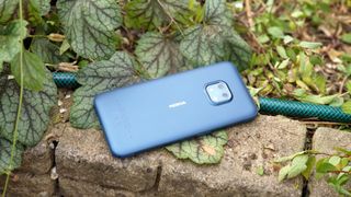 Bästa robusta mobiler: En blå Nokia XR20 ligger på en stenkant bland gröna växter utomhus med baksidan vänd uppåt mot kameran.