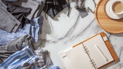 Files of clothes on a white marble table with a cup of coffee and an open notebook with pen