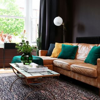 a living room with a tan leather sofa, colourful cushions and coffee table