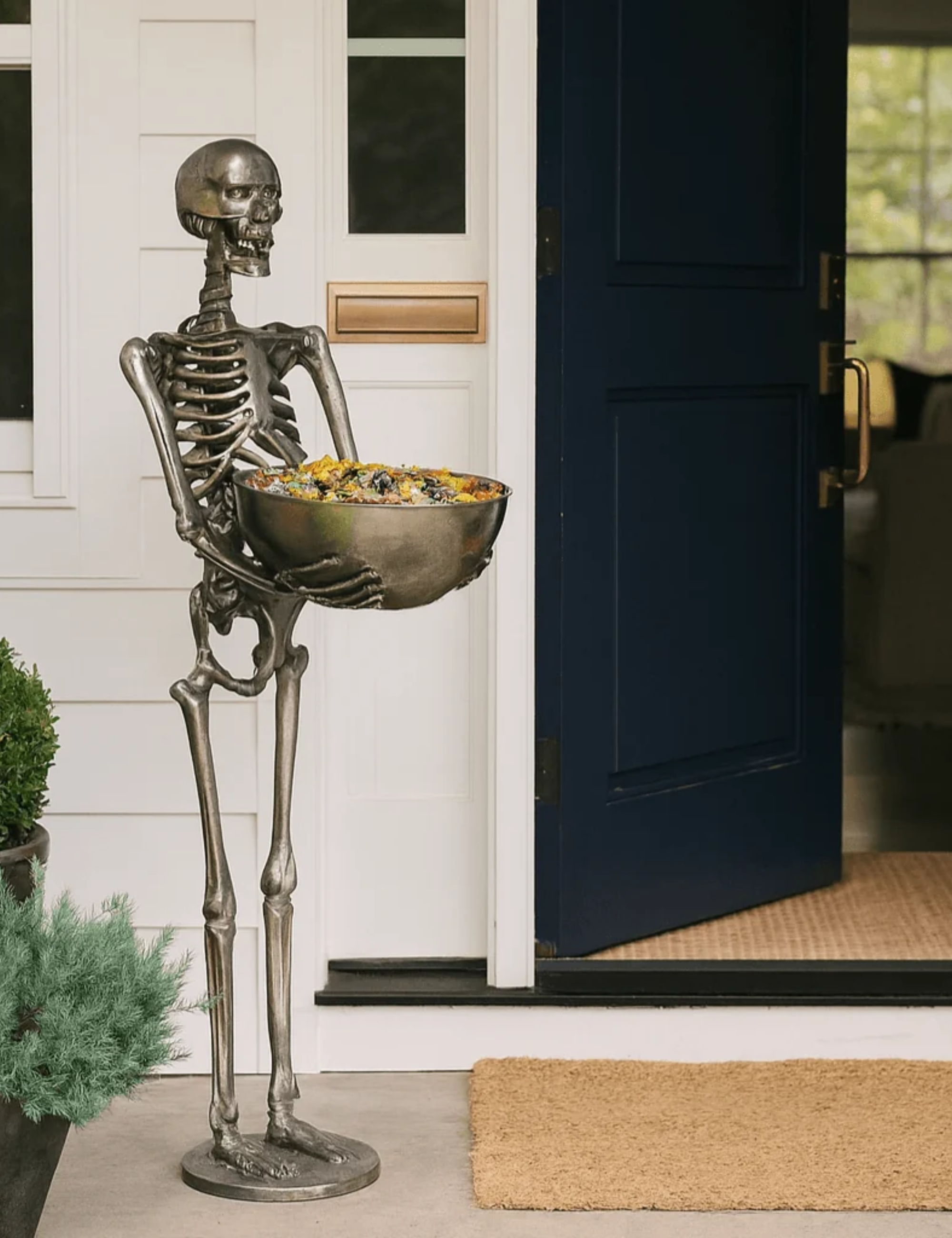 Standing chrome skeleton serving bowl holding candy outside of a charming navy front door